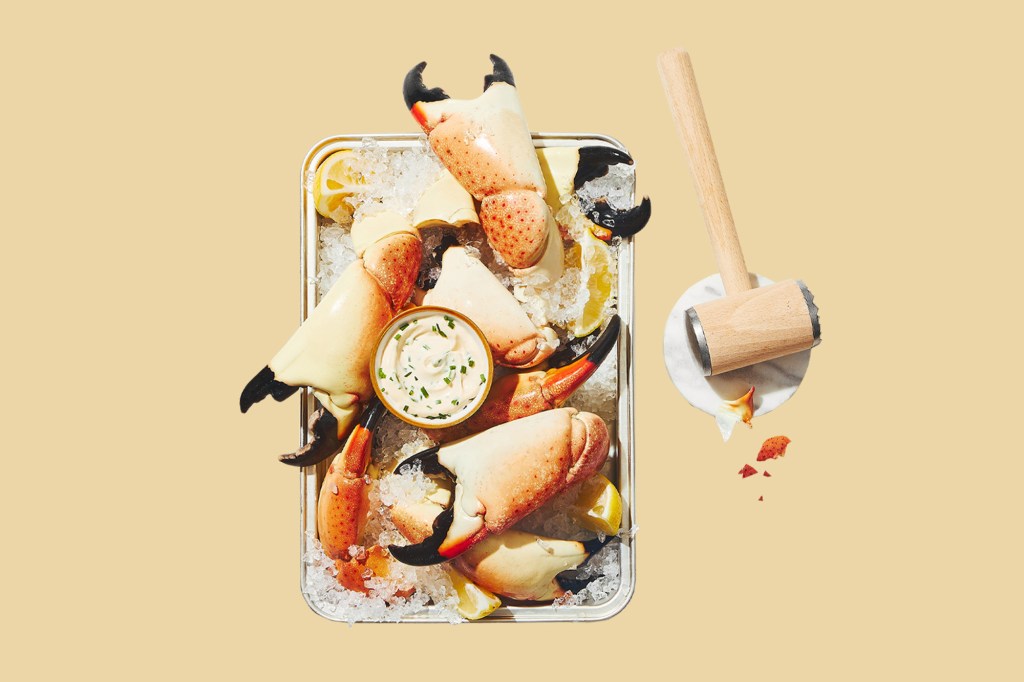 A tray of crab claws accompanied by a sauce and a wooden mallet